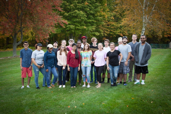 group of students standing together outside in front of fall foliage, smiling at camera