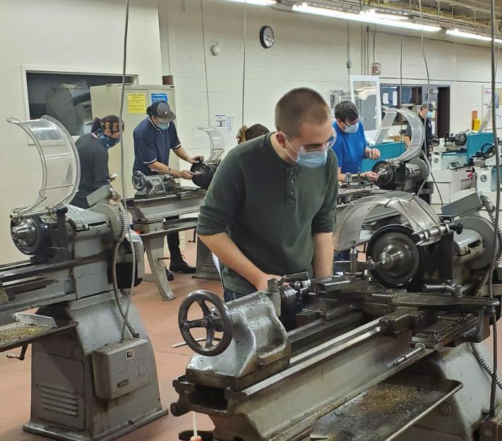 masked students working on manufacturing equipment