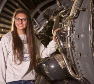 Girl standing by large machinery and smiling at camera